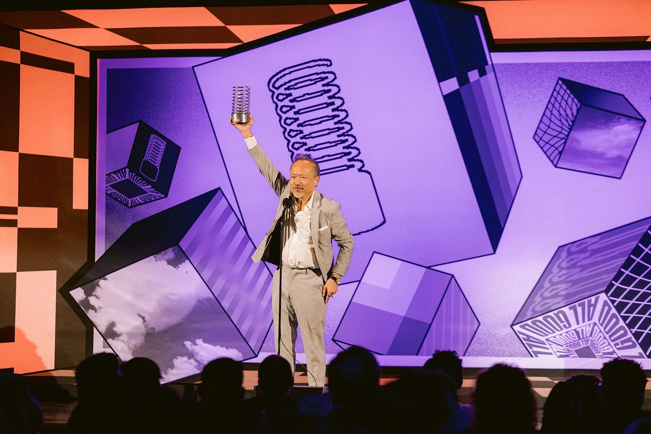Robert Wong of Google hoists a Webby trophy above his head while standing on stage.